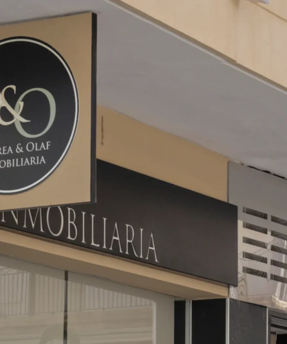 Außenbeschilderung der Immobilienagentur Andrea & Olaf mit kreisförmigem Logo an einer Fassade aus schwarzem Stein und Glasfront.