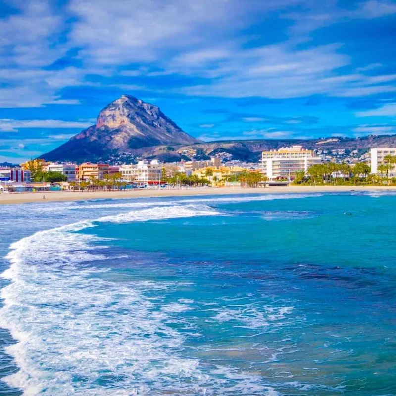 Panoramablick auf den Strand von Jávea mit dem Montgó im Hintergrund. Wohngebäude säumen die Küste.