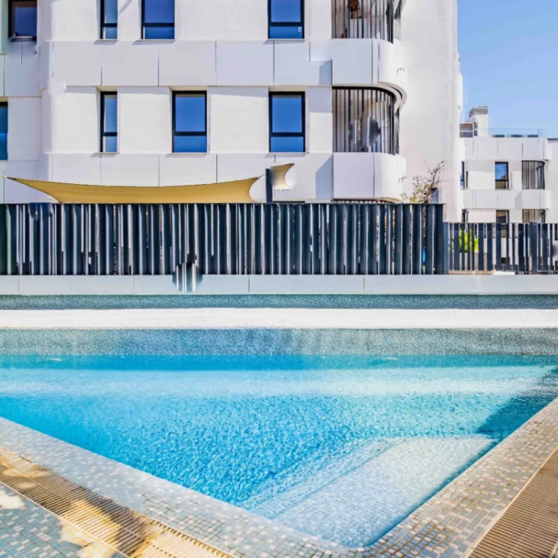 Gemeinschaftlicher Pool mit blauen Mosaikfliesen und integrierter Treppe, umgeben von einem modernen Sicherheitszaun und zeitgenössischer Architektur in Jávea.
