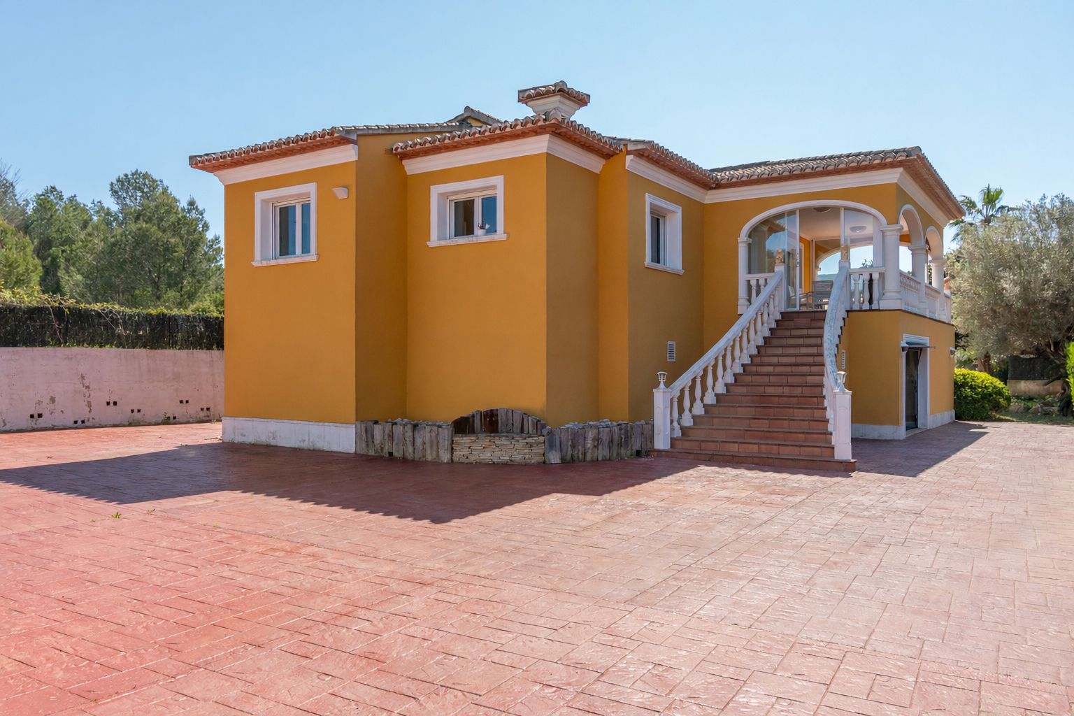Außenansicht der ockerfarbenen Villa mit einer prachtvollen Treppe, weißer Balustrade und einer großzügigen, terrakottafarbenen Einfahrt aus Stempelbeton.
