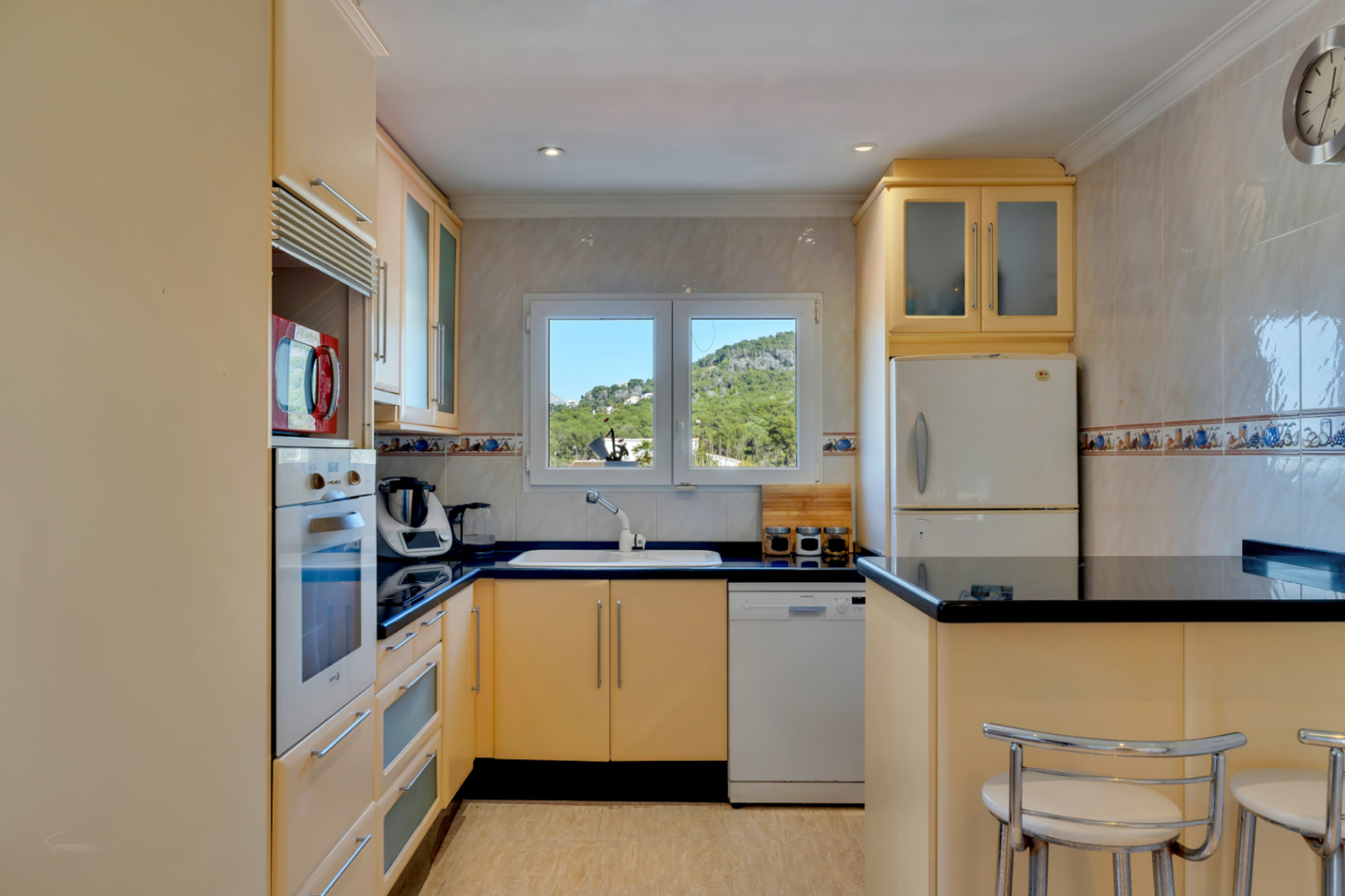 Funktionale Küche mit cremefarbenen Schränken, schwarzen Granitarbeitsplatten und Fenster mit Bergblick. Ausgestattet mit integrierten Geräten und Frühstückstheke.