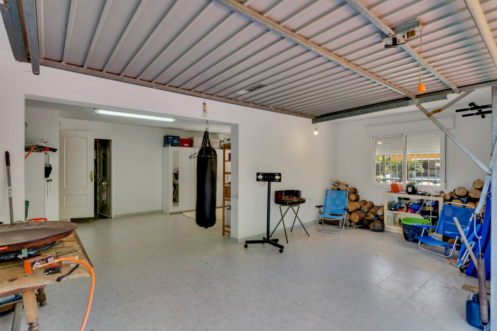 Großzügige Mehrzweckgarage mit Metalldecke und Fliesenboden. Vielseitiger Raum für Lagerung, Fitnessbereich und Brennholz mit direktem Hauszugang.