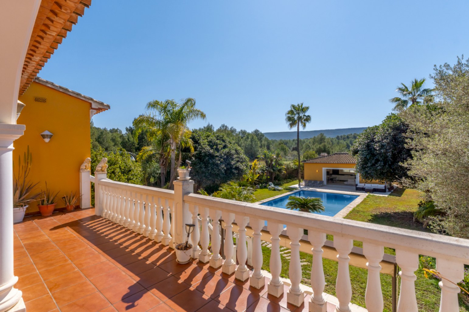Obere Terrasse mit weißer Balustrade und Terrakottafliesen, mit Blick auf den 15x6 m großen Pool, den mediterranen Garten und die angrenzende Naturlandschaft.