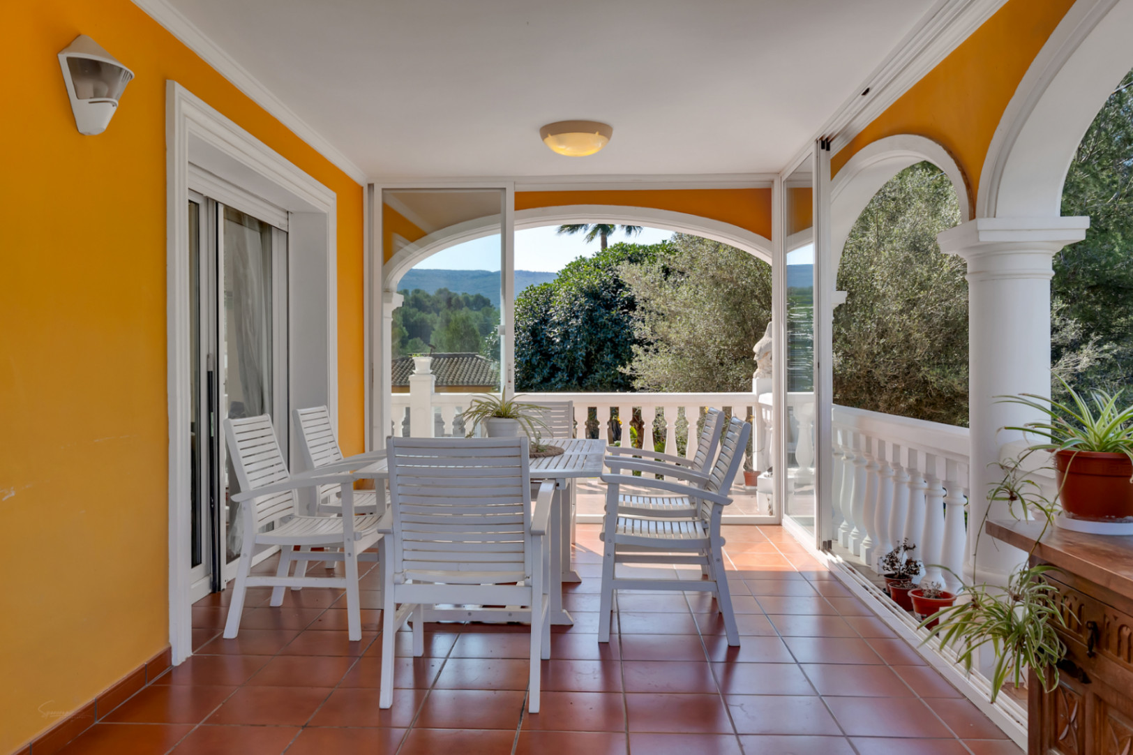 Überdachte Terrasse mit Essbereich, Terrakottaboden und Glasfronten, die einen weiten Blick auf die umliegende Natur und die Berge ermöglichen.