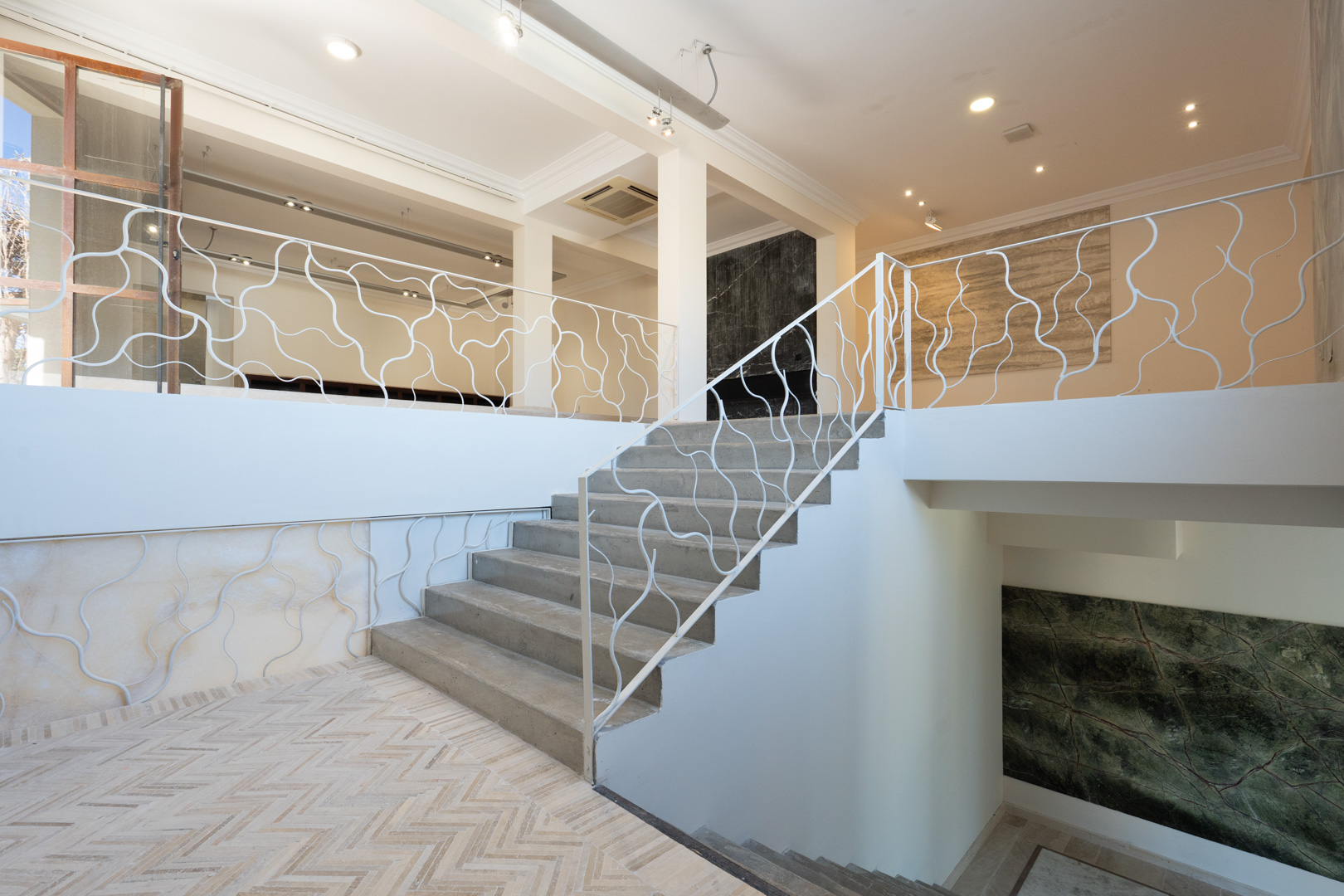 Architektonische Treppe mit organisch geformtem weißem Geländer, die die Gewerbeebenen verbindet, mit Fischgrätboden und dekorativen Steinpaneelen.