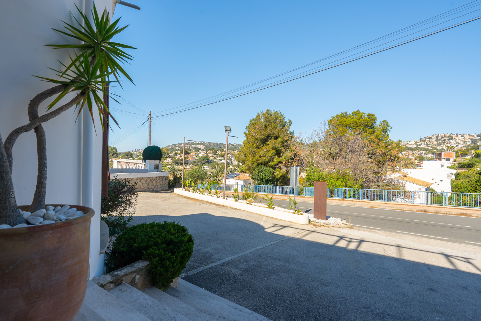 Außenparkplatz und Haupteingang mit hoher Sichtbarkeit von der Straße, mediterraner Bepflanzung und weitem Blick auf die umliegenden Hügel.