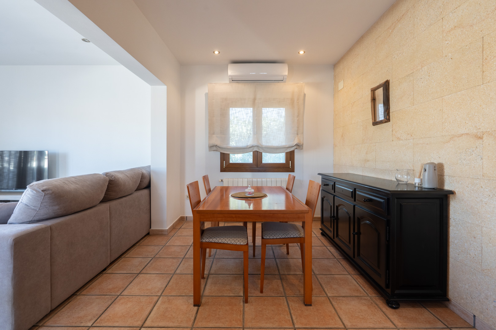 Essbereich mit Natursteinwand, rustikalen Fliesenböden, Holztisch für vier Personen und schwarzem Sideboard. Inklusive Klimaanlage und Heizkörper.
