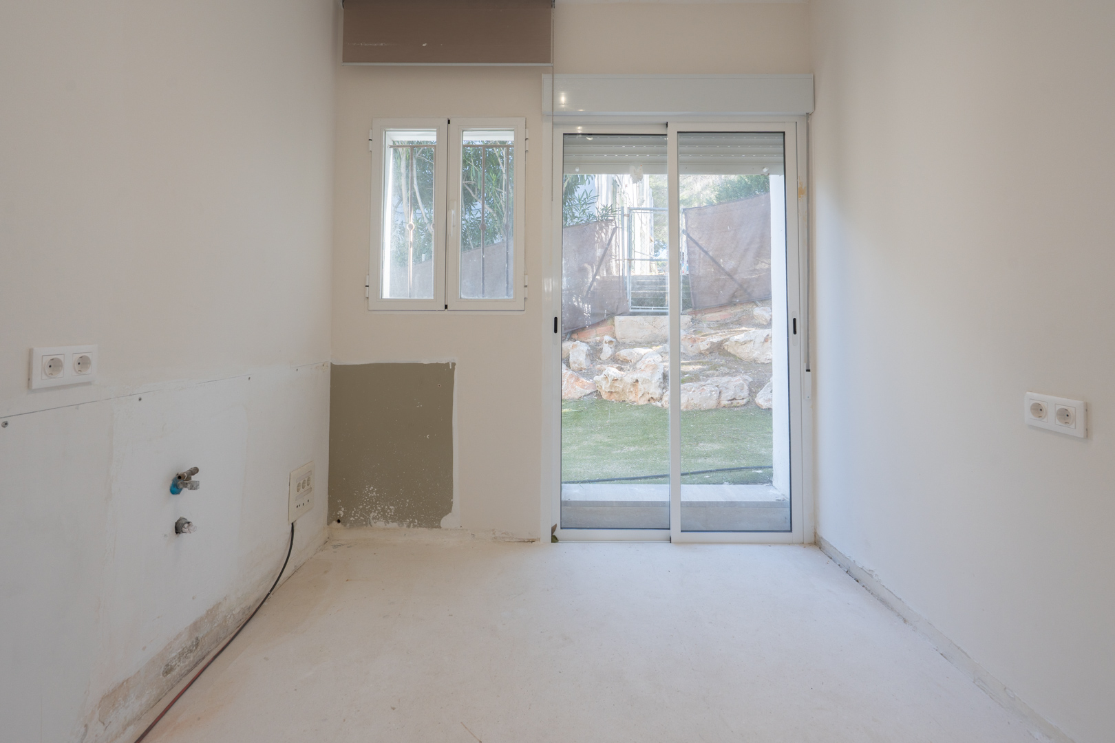 Heller Raum mit Sanitärvorinstallationen, weißen Aluminiumrahmen und einer Glasschiebetür, die direkt in den Außenbereich führt.
