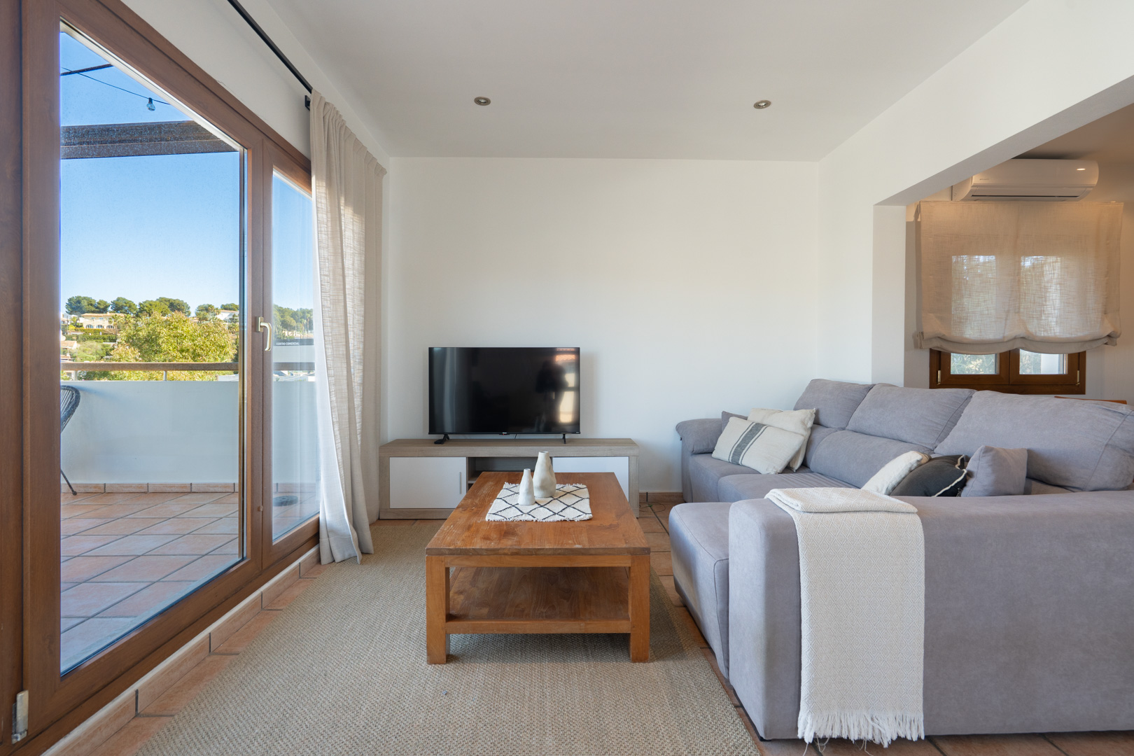 Helles Wohnzimmer mit grauem Ecksofa, Couchtisch aus Holz und direktem Zugang zur Terrasse durch große Glasschiebetüren mit Holzrahmen.