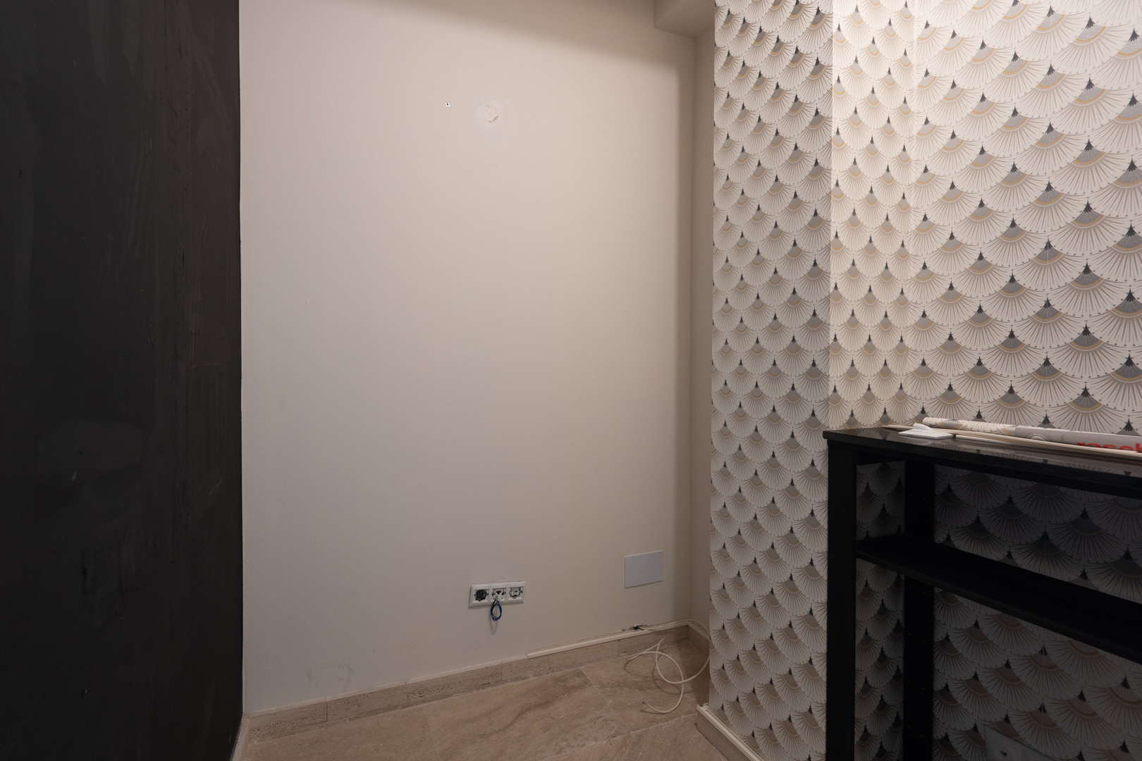 Innenbereich mit geometrisch gemusterter Tapete, neutralen weißen Wänden mit Steckdosen und hellem Natursteinboden.