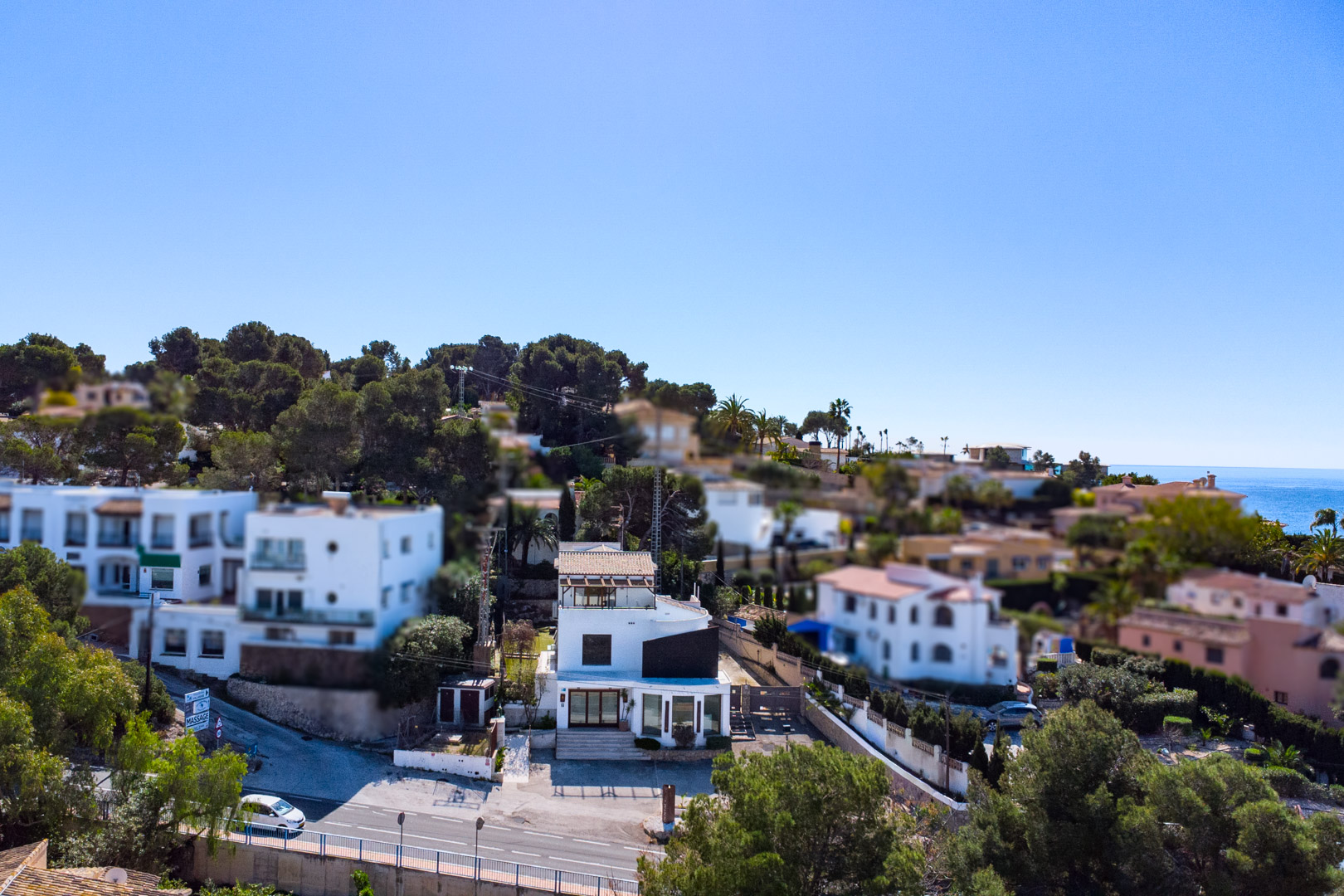 Luftaufnahme der Immobilie an der Straße Moraira-Calpe mit weißer Fassade, großen Schaufenstern und Blick auf das nahegelegene Mittelmeer.