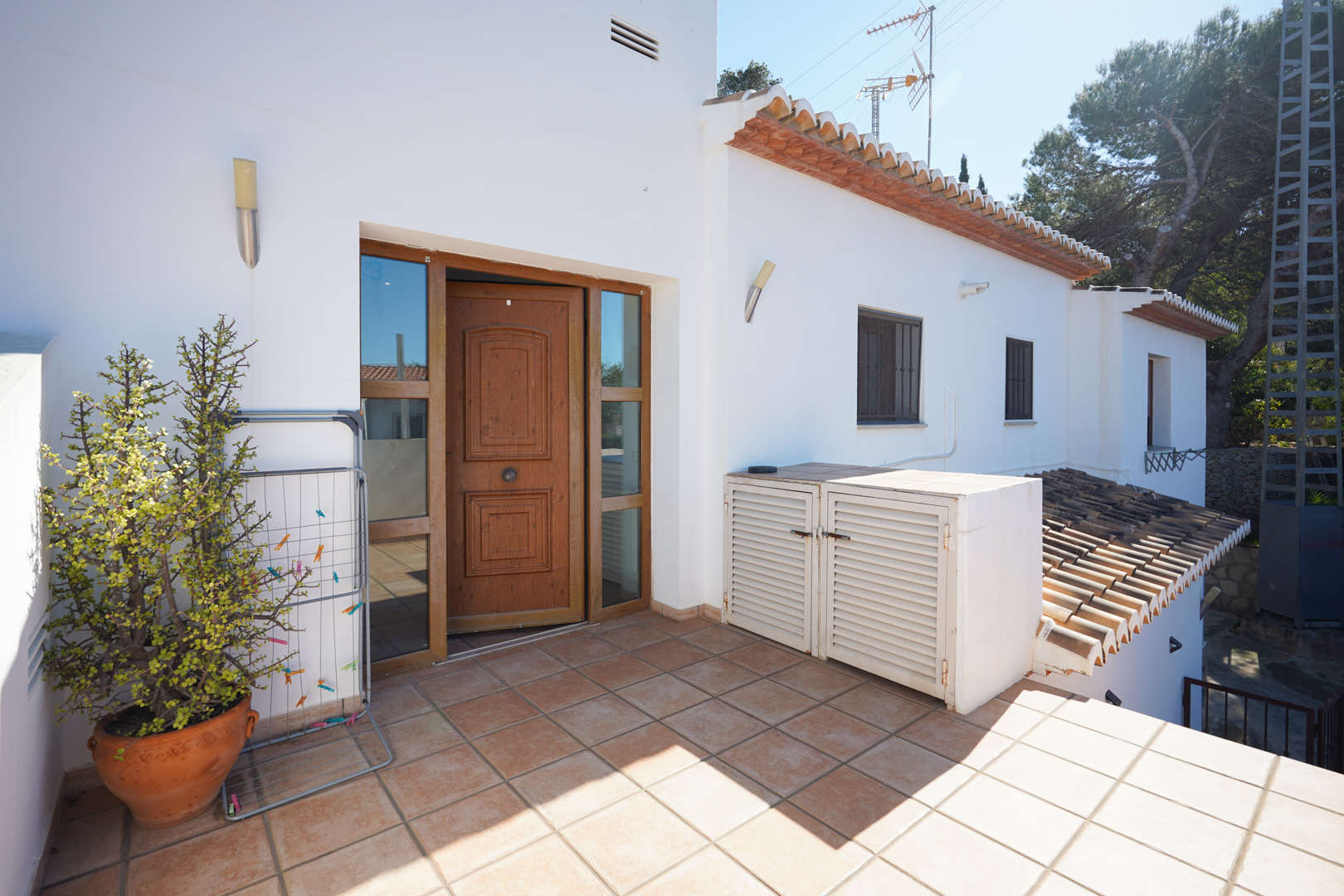 Privater Zugang zum Obergeschoss mit einer terracotta-gefliesten Terrasse, einer Holztür mit Glaselementen und klassischen weiß getünchten Wänden.