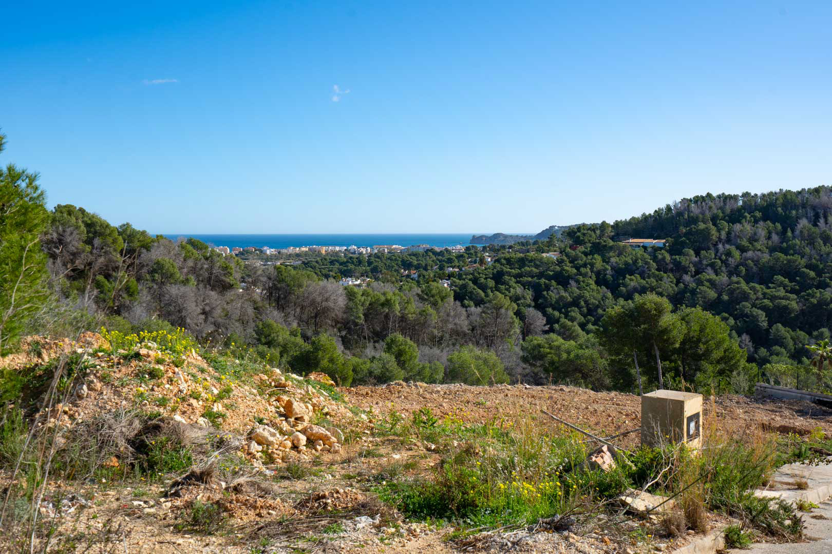 Panoramablick auf das Meer und die Küste vom erhöhten Grundstück aus, umgeben von einem dichten mediterranen Pinienwald und weiter Naturlandschaft.