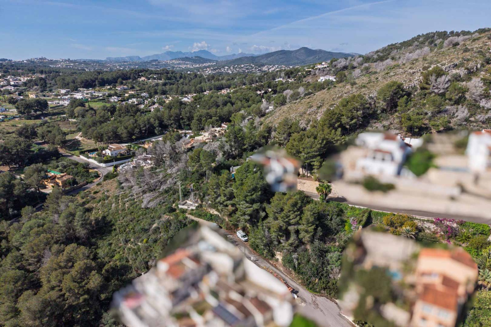 Luftaufnahme der Urbanisation Sol de Este mit Blick auf dichte Pinienwälder, die umliegenden Hügel und ferne Bergketten unter klarem blauem Himmel.