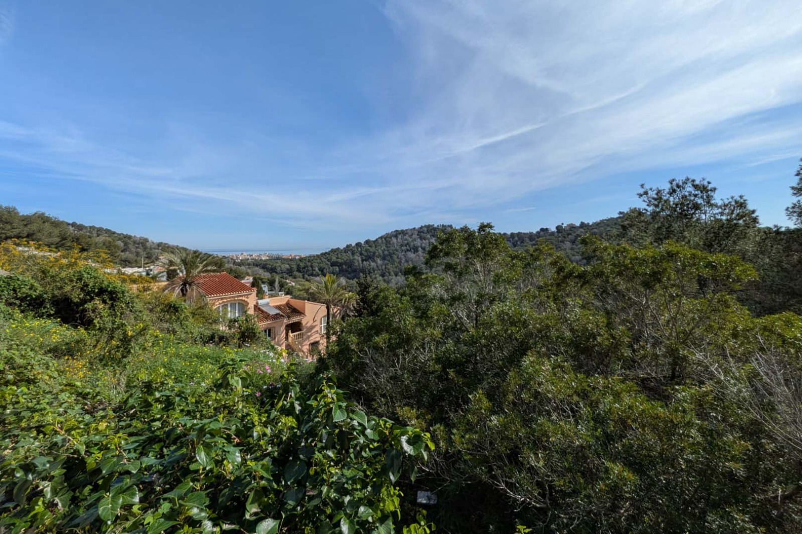 Panoramablick vom Grundstück auf das Mittelmeer und die bewaldeten Hügel, mit dichter mediterraner Vegetation und Villen im traditionellen Stil.