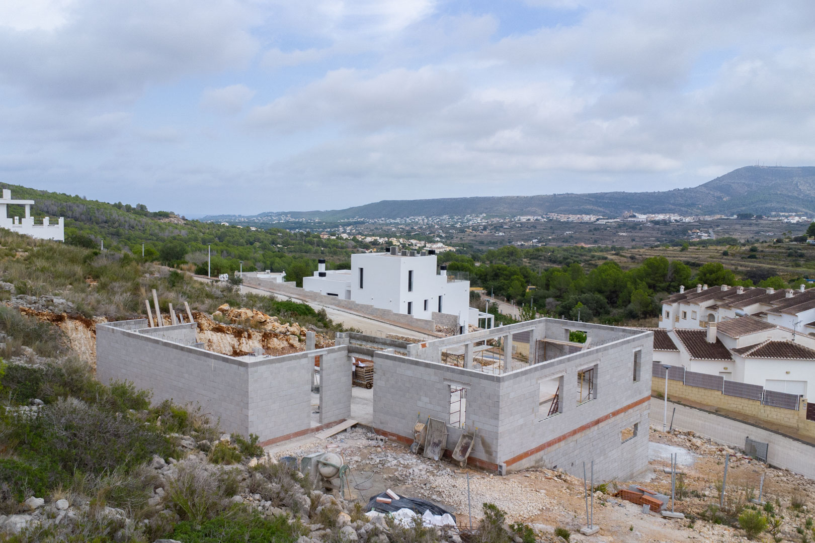 Bauphase einer modernen Villa in Pedreguer mit Rohbau aus Betonsteinen und Panoramablick auf das Tal und die umliegende Berglandschaft.