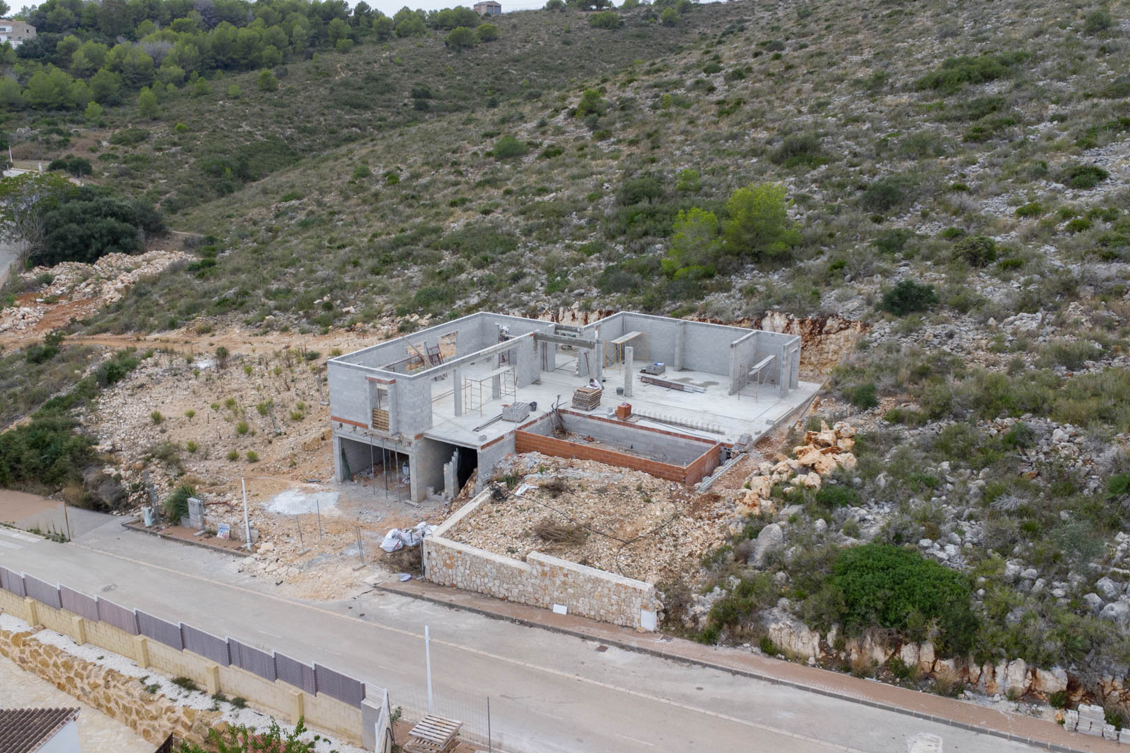 Luftaufnahme des Baufortschritts der Villa in Pedreguer mit dem Rohbau aus Betonsteinen und dem in den natürlichen Hang integrierten Fundament.