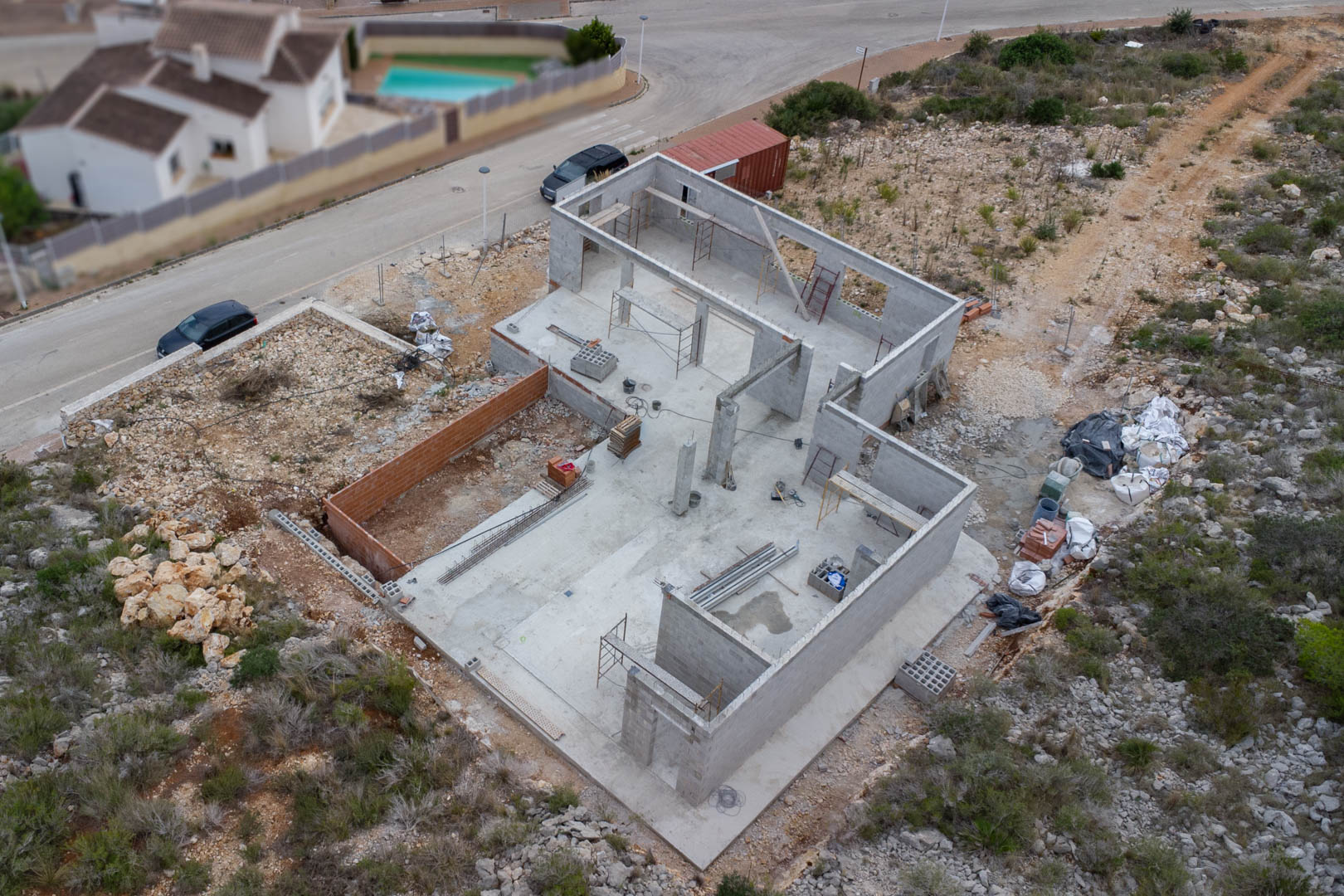 Luftaufnahme des Betonfundaments und der Blockwandstruktur der im Bau befindlichen Villa mit Baumaterialien und Gerüsten auf dem Grundstück.