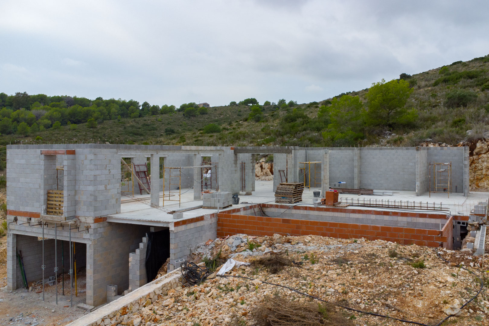 Moderne Villa im Bau in Pedreguer mit Betonblockwänden, Poolstruktur und erhöhter Hanglage inmitten mediterraner Vegetation.