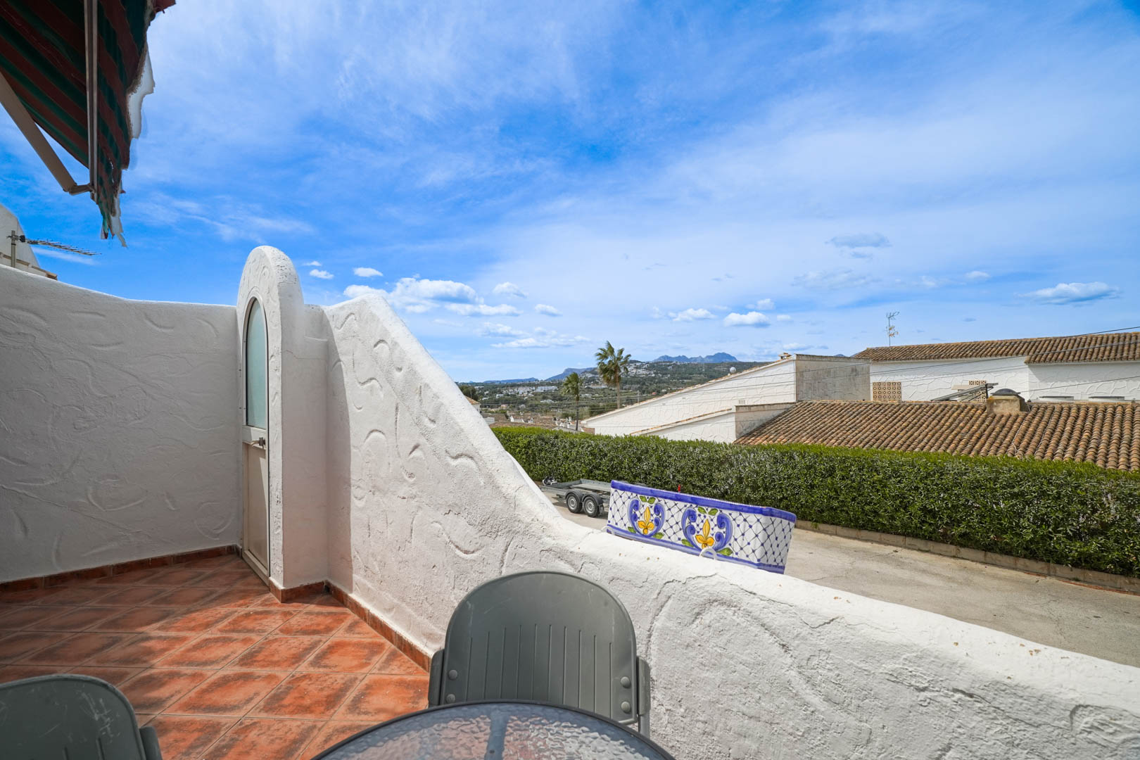 Hochgelegene Terrasse mit rustikalen Fliesen und weitem Talblick. Der Außenbereich umfasst einen integrierten Abstellraum und charakteristische weiße Mauern.