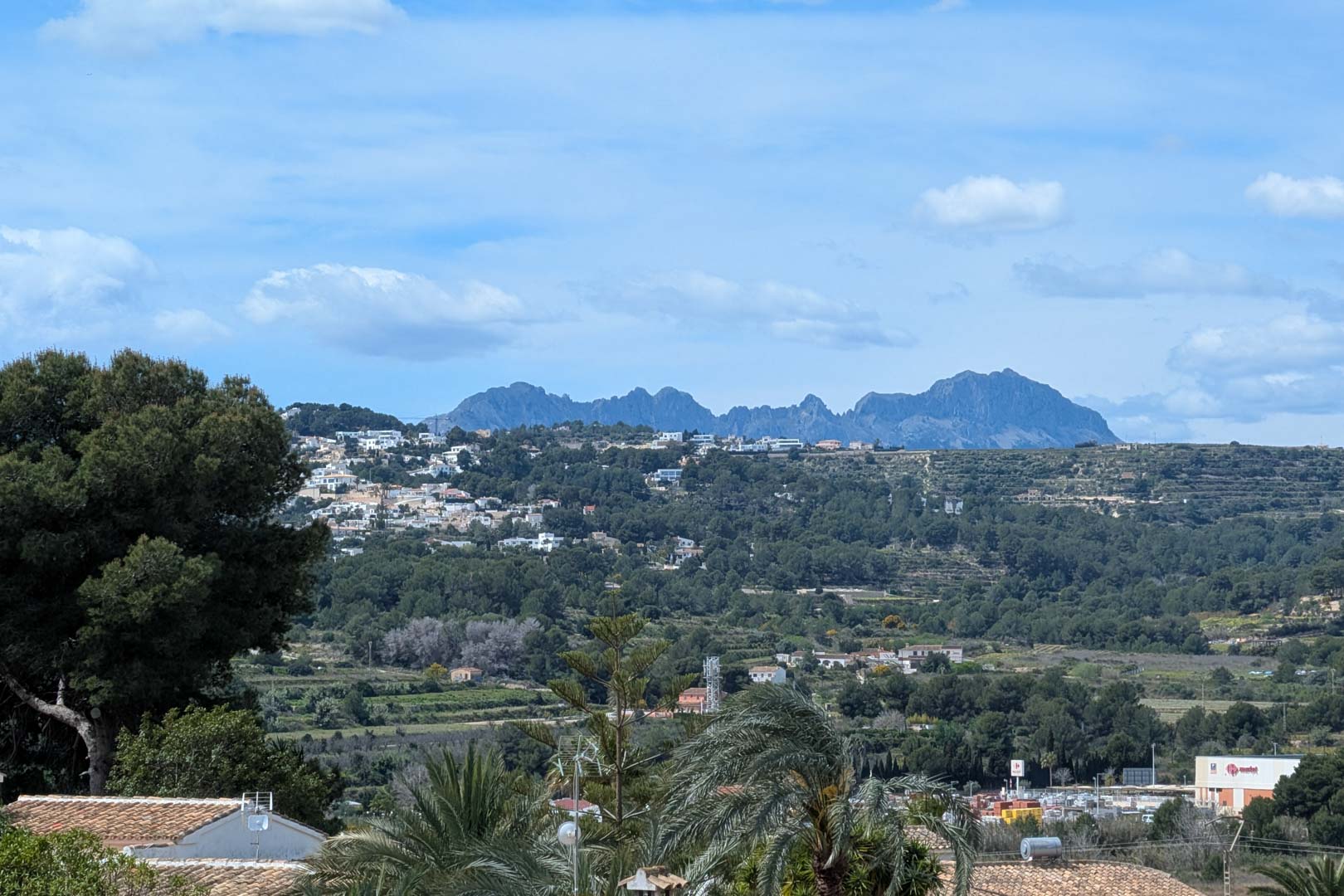 Panoramablick von der Terrasse auf das Tal und die Bergkette, mit mediterraner Vegetation und der Wohnlandschaft von Moraira unter klarem Himmel.