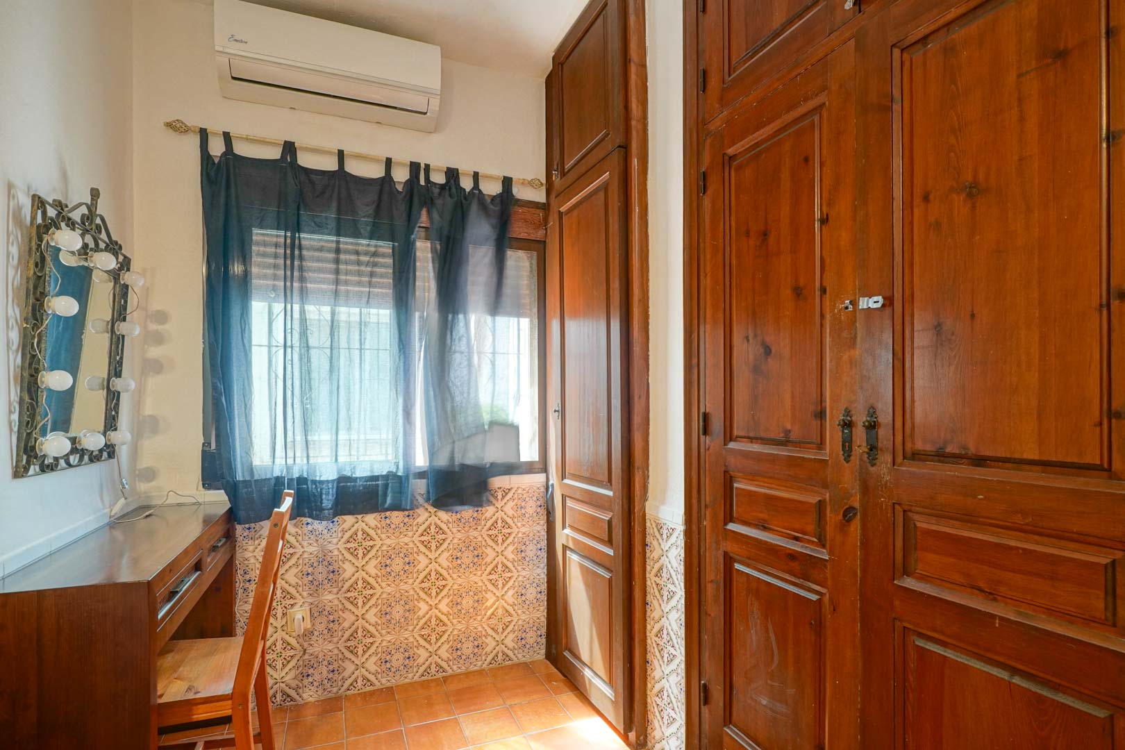 Schminkecke mit Schreibtisch aus Holz und beleuchtetem Spiegel, neben großen Einbauschränken aus dunklem Holz und traditionell gemusterten Wandfliesen.