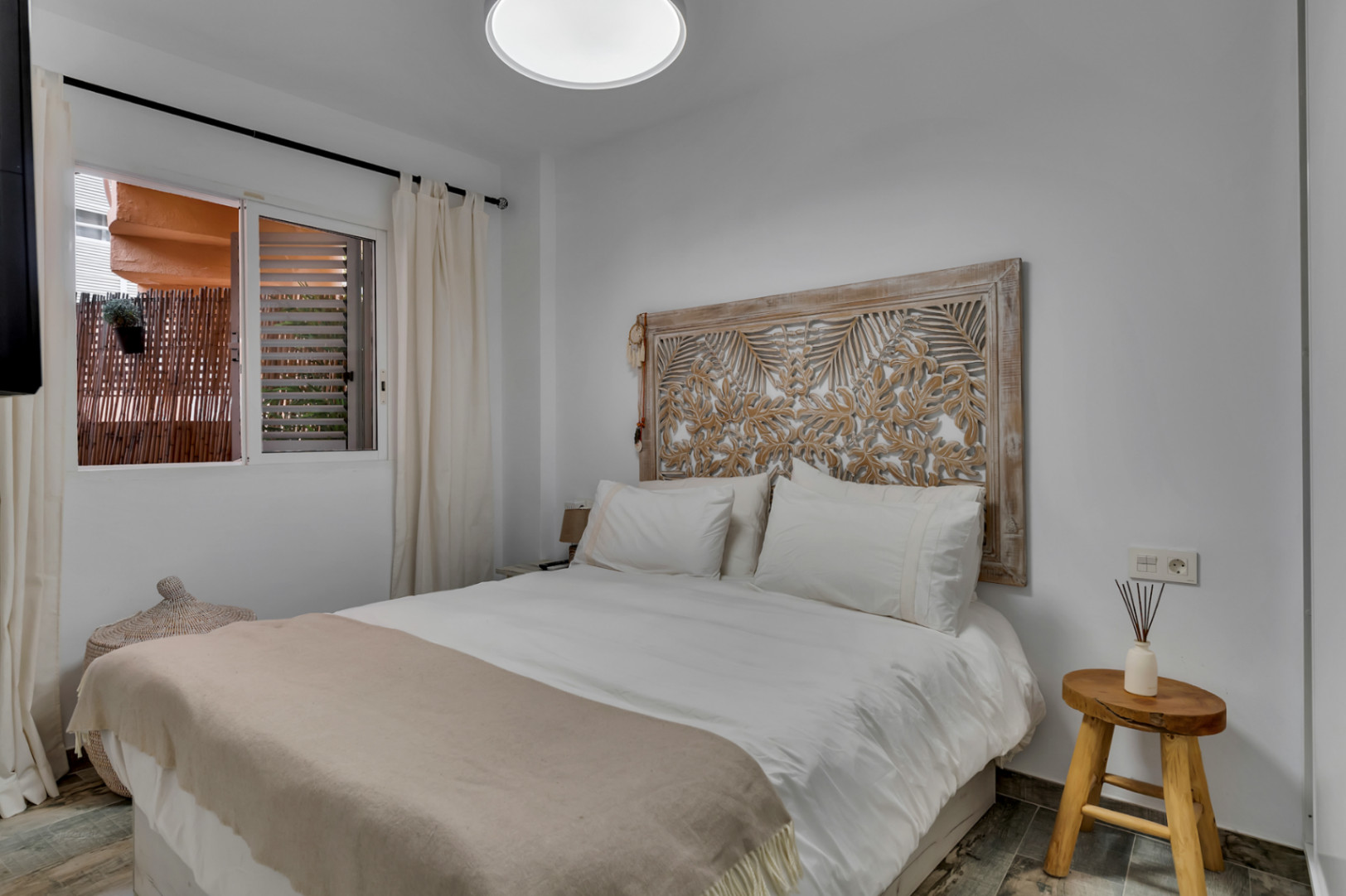 Helles Schlafzimmer mit geschnitztem Holzkopfende und Blick auf die Terrasse.
