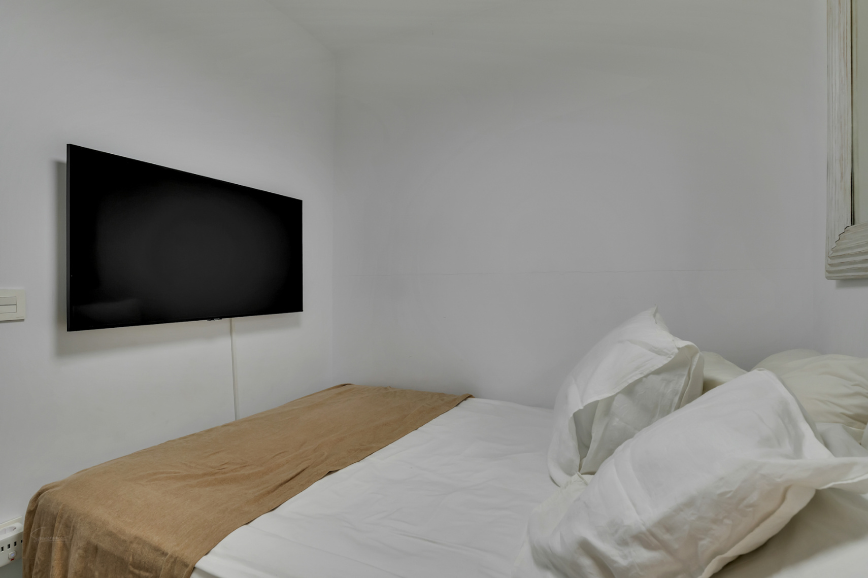 Schlafzimmerdetail mit Flachbildfernseher und weißer Bettwäsche.