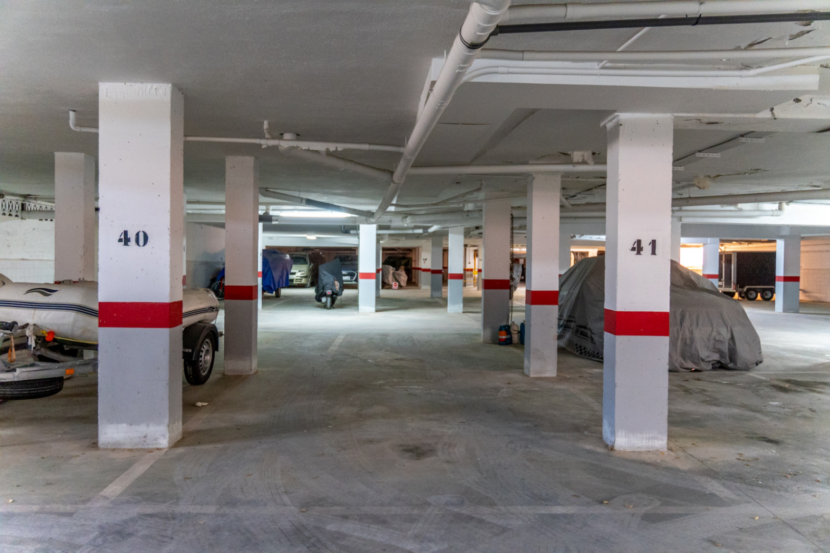 Tiefgarage mit nummerierten Säulen und abgedeckten Fahrzeugen.