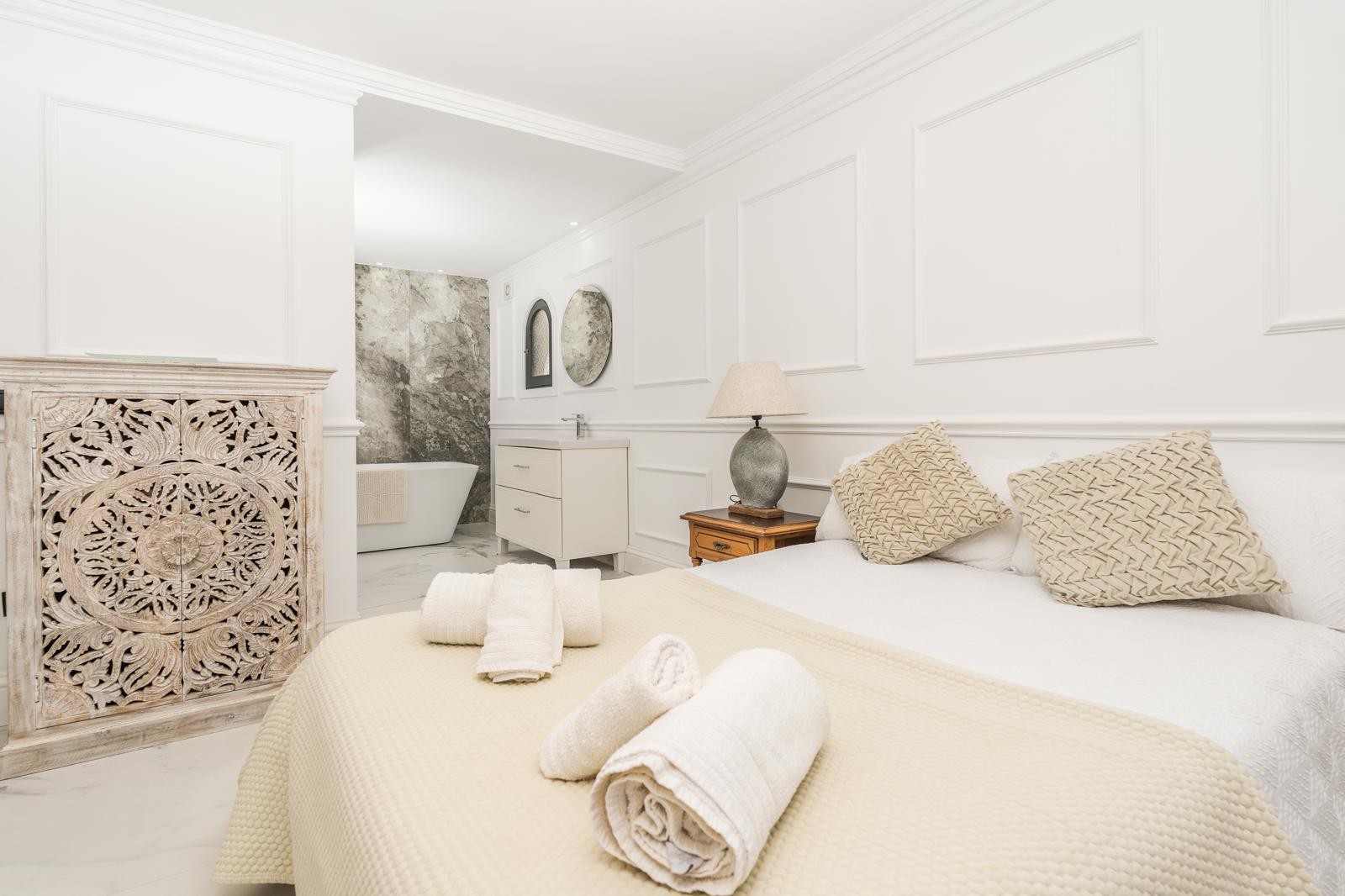 Hauptschlafzimmer mit dekorativen Wandleisten, handgeschnitztem Holzschrank und offenem Bad mit freistehender Badewanne und Marmorwänden.