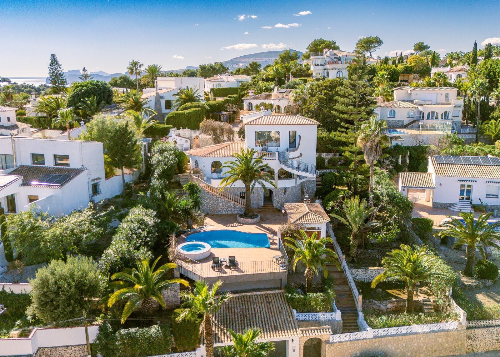 Luftaufnahme der Villa mit drei Ebenen, Pool und integriertem Whirlpool, Natursteinmauern, Außentreppe und einem gepflegten mediterranen Garten mit Palmen in Jávea.
