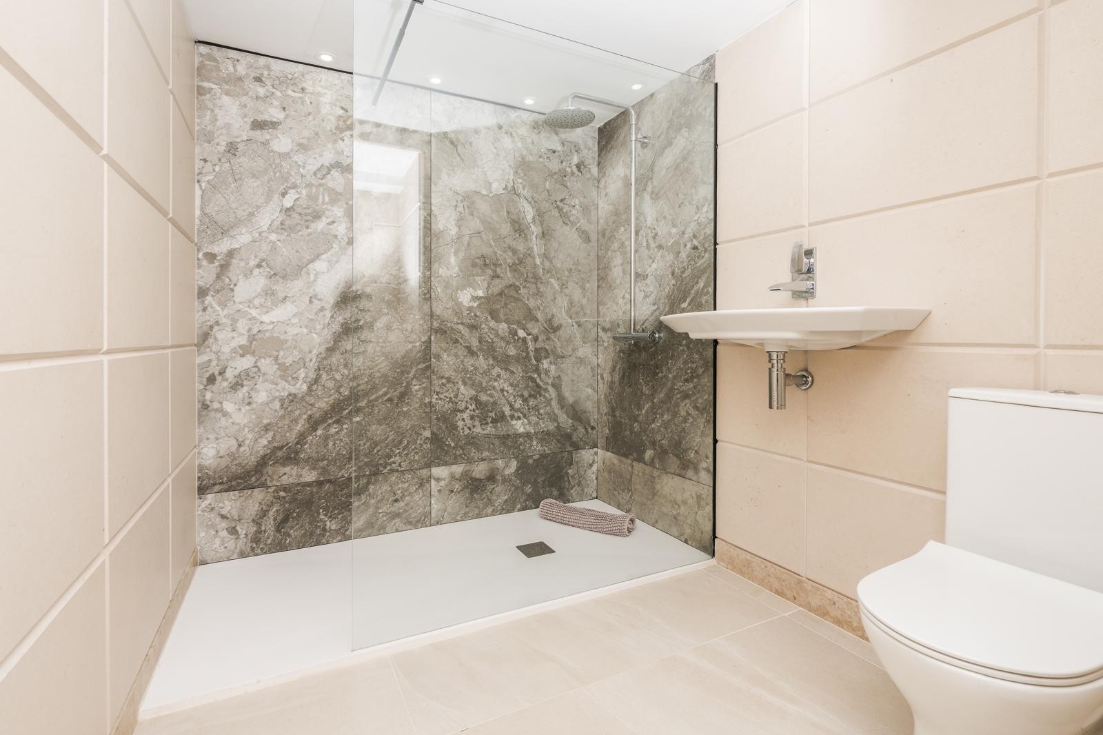Modernes Badezimmer mit begehbarer Dusche, grauen Marmorfliesen, einer Glasduschwand und dezenter Deckenbeleuchtung.