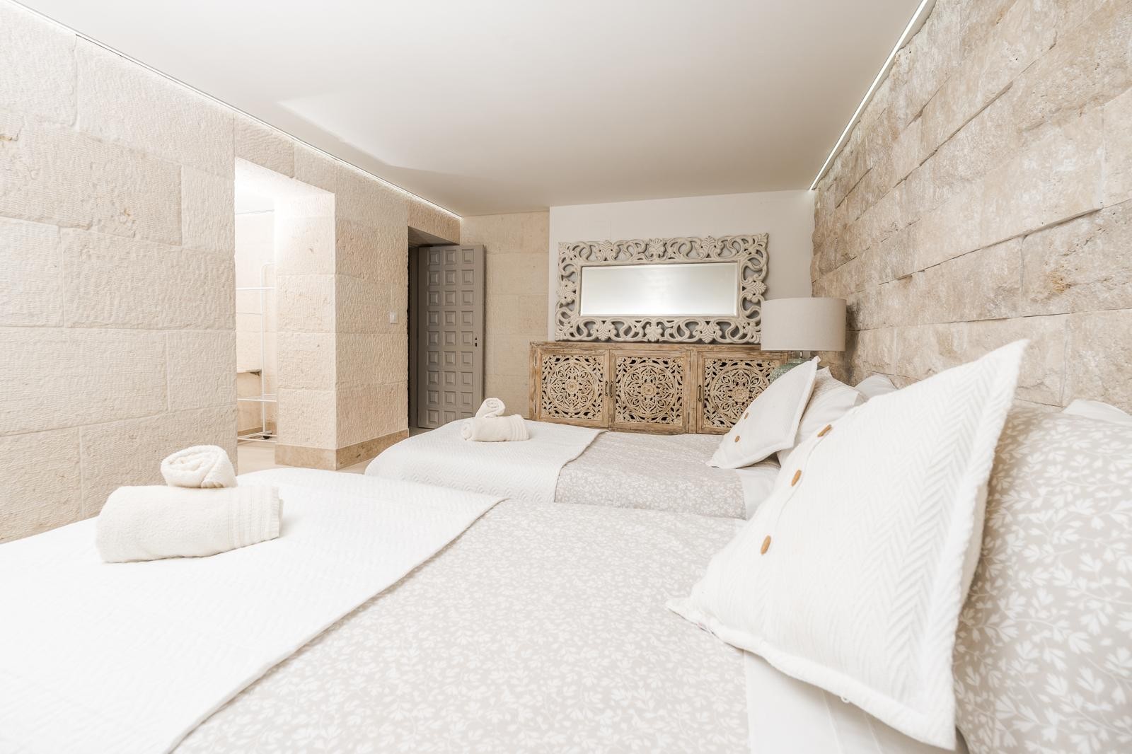 Schlafzimmer mit Wänden aus Naturstein, handgeschnitzten Holzmöbeln und indirekter LED-Deckenbeleuchtung für ein elegantes, ruhiges Ambiente.