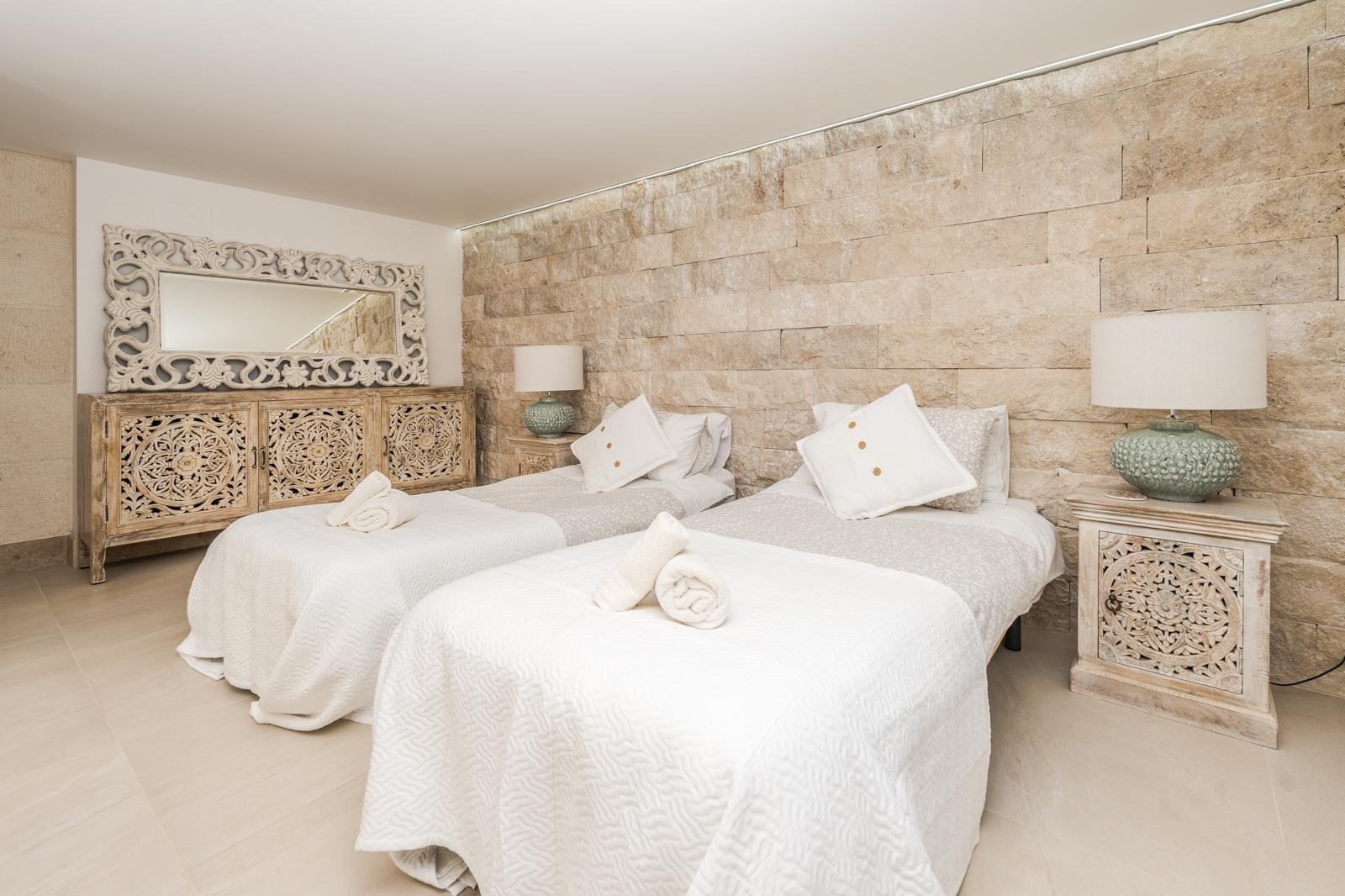 Schlafzimmer mit zwei Einzelbetten, einer markanten Natursteinwand und handgeschnitzten Holzmöbeln im mediterranen Stil.