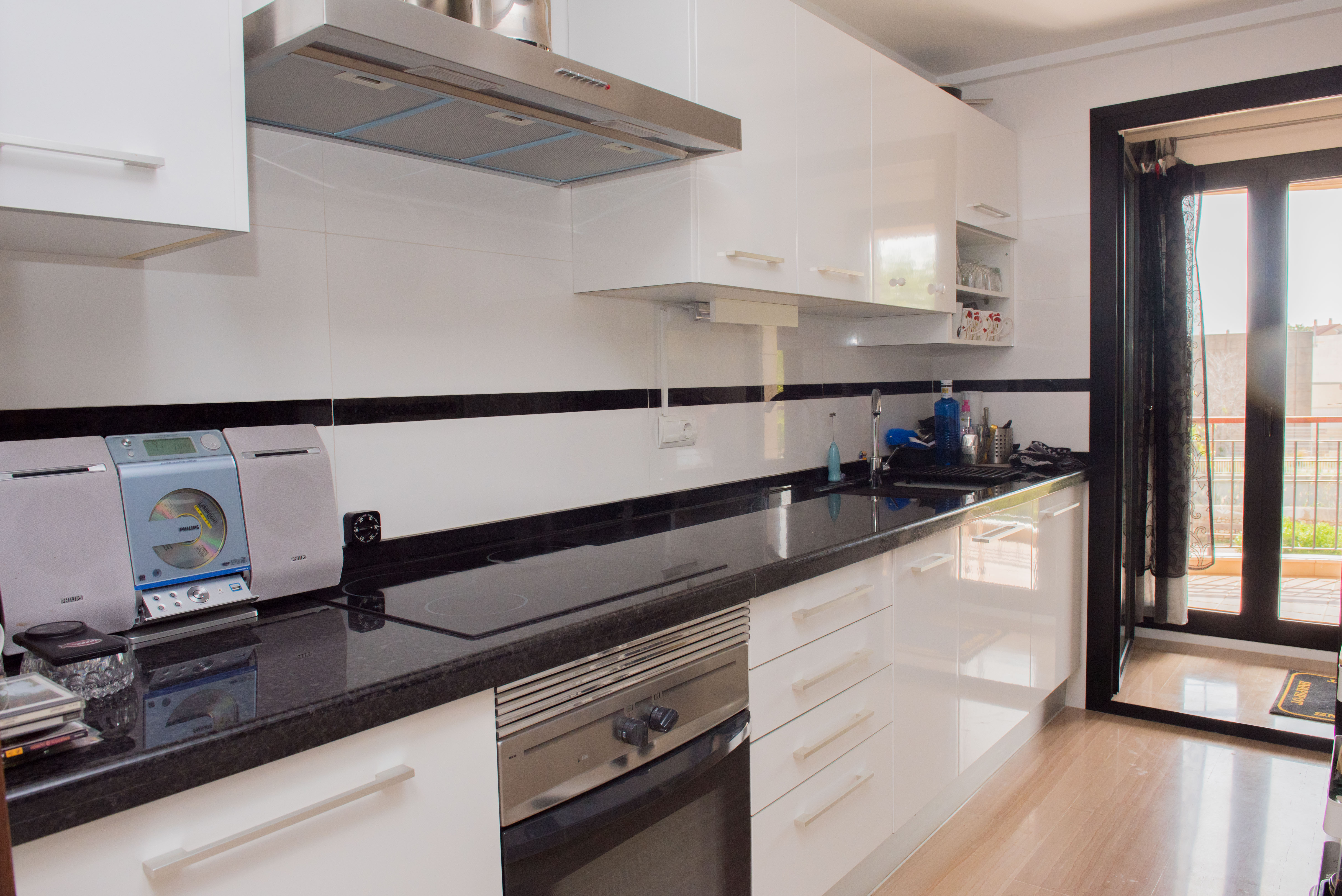 Moderne Küche mit weißen Hochglanzfronten, schwarzer Granitarbeitsplatte und Edelstahlofen. Ein direkter Zugang führt auf den angrenzenden Balkon.