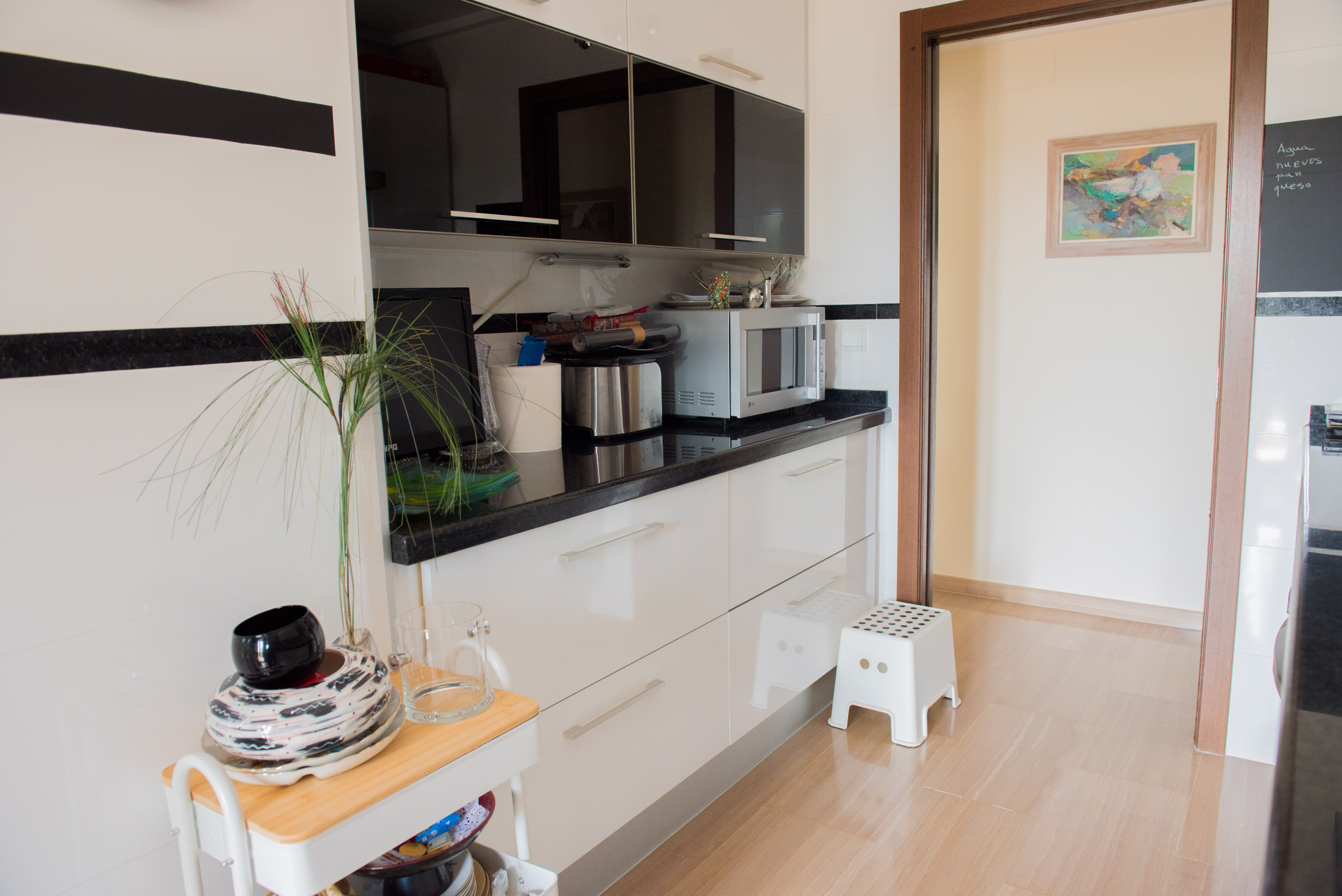 Moderne Küche mit weißen Hochglanzschränken, schwarzen Glasoberflächen und dunkler Granitarbeitsplatte. Heller Holzboden ergänzt das zeitgemäße Design.