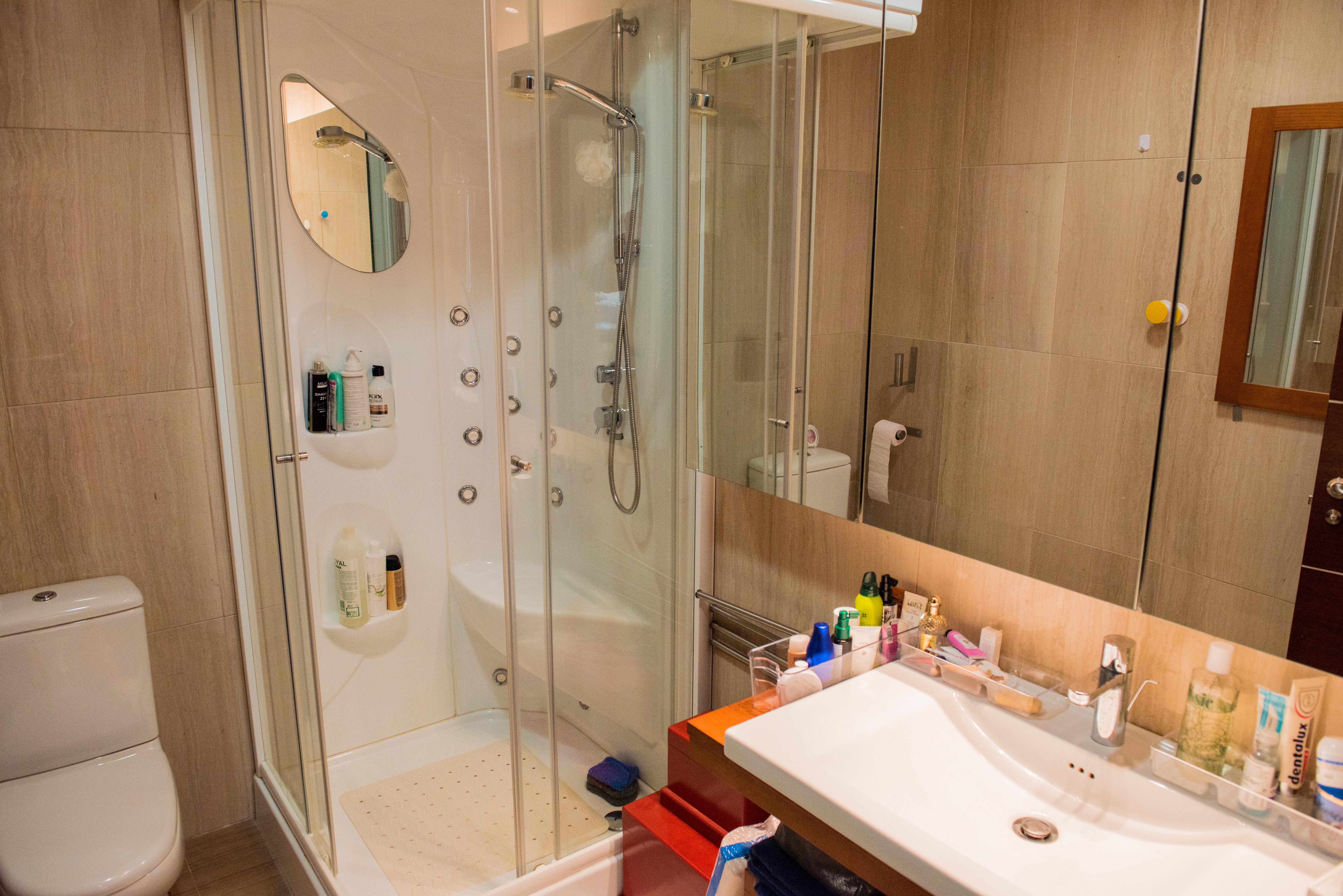 Modernes Badezimmer mit Hydromassage-Duschkabine, Glastüren, weißem Design-Waschbecken und neutralen Feinsteinzeugfliesen an den Wänden.