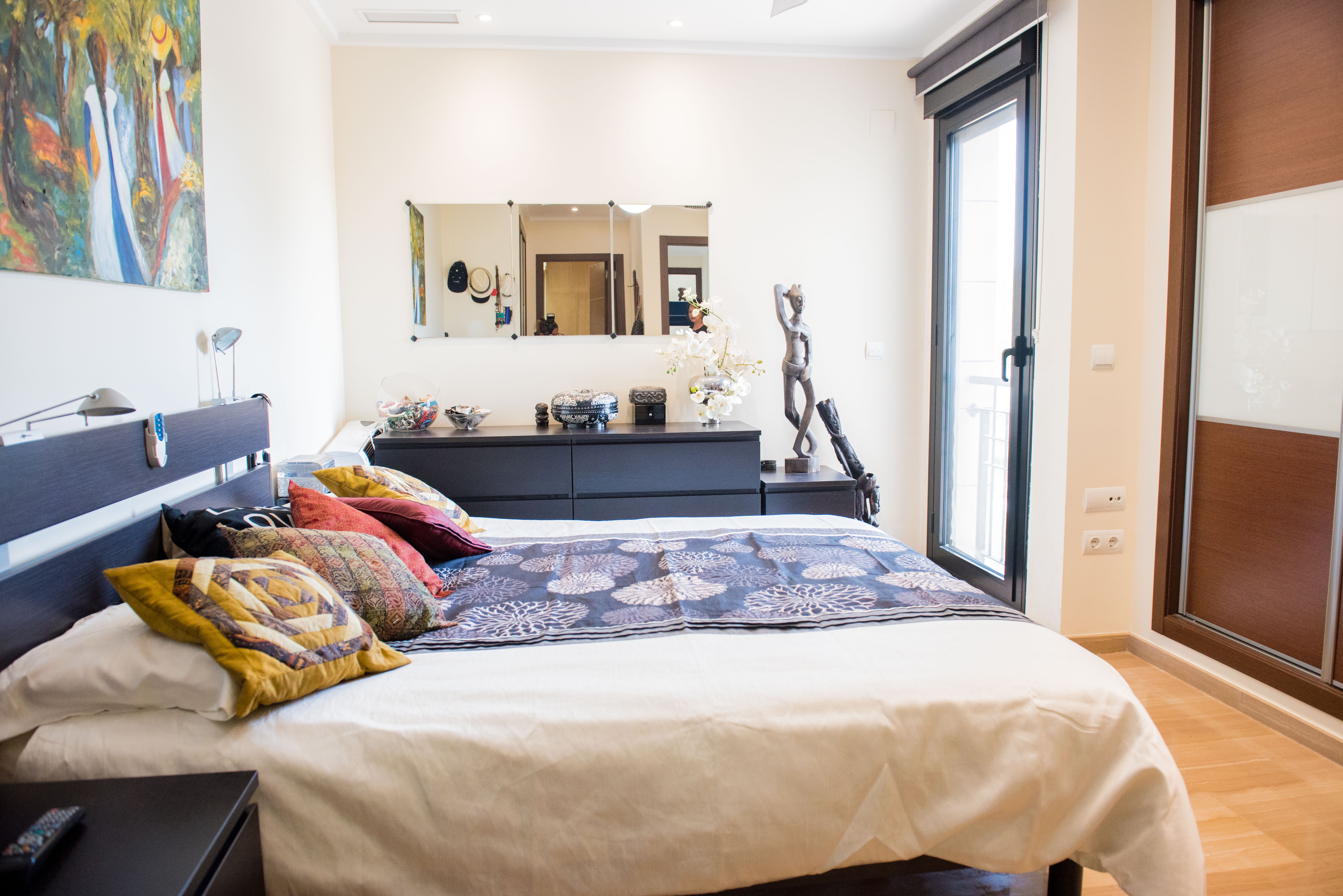 Schlafzimmer mit dunklen Holzmöbeln, Einbauschränken und Glastür für natürliches Licht. Der Raum bietet eine Kommode mit Spiegel und hellen Holzfußboden.