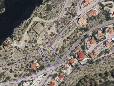 Luftaufnahme des blau umrandeten Stadtgrundstücks, gelegen an der Straße 'ROMER' innerhalb der Urbanisation Monte Pedreguer. Das unbebaute Gelände ist von bestehenden Wohnimmobilien umgeben.