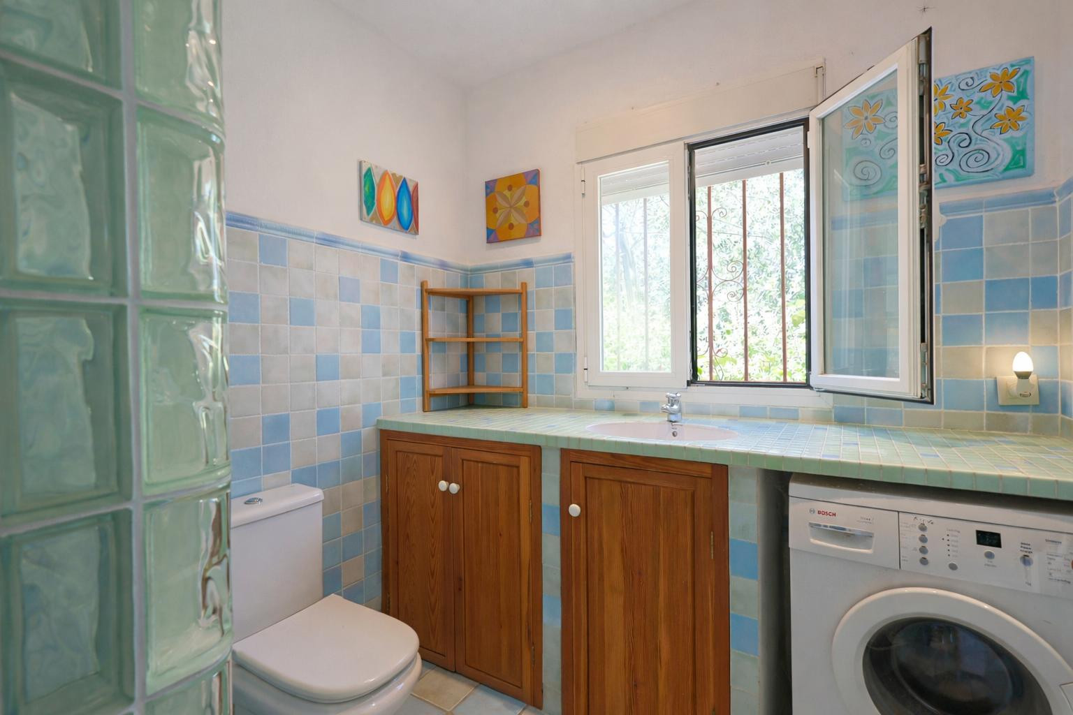 Funktionales Badezimmer mit blauen Fliesen, gefliester Arbeitsplatte mit integriertem Waschbecken, Holzschränken und hellem Waschmaschinenplatz.