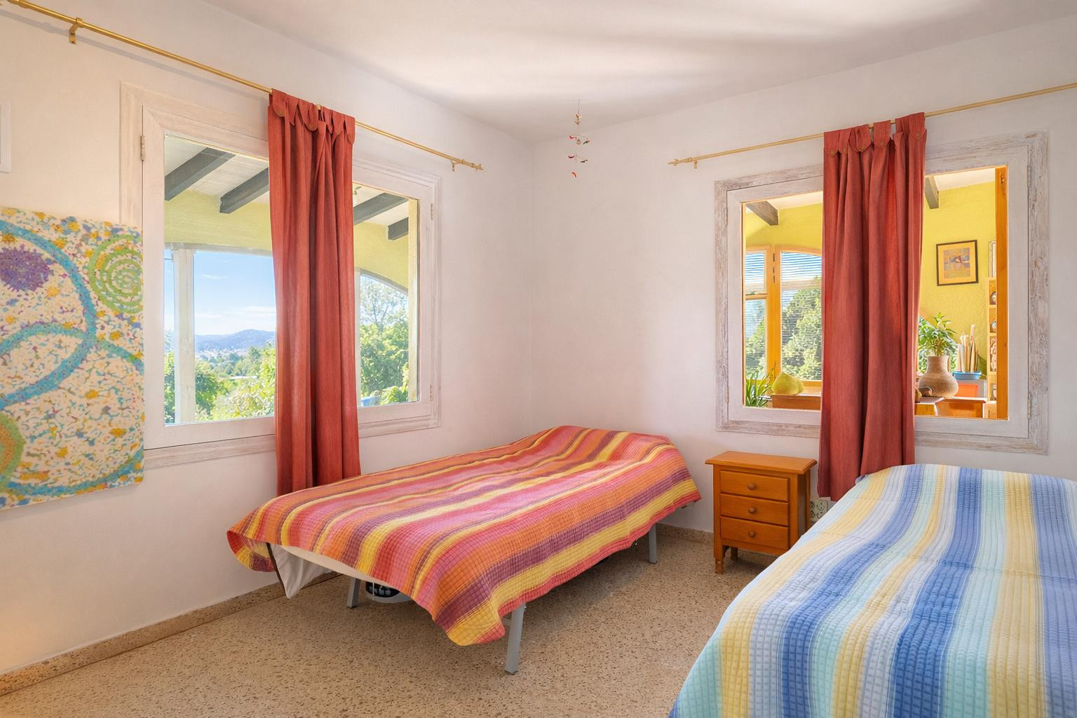 Helles Schlafzimmer mit zwei Einzelbetten, einem Holznachttisch und weißen Fensterrahmen, die Ausblicke auf die Landschaft und den Innenbereich bieten.