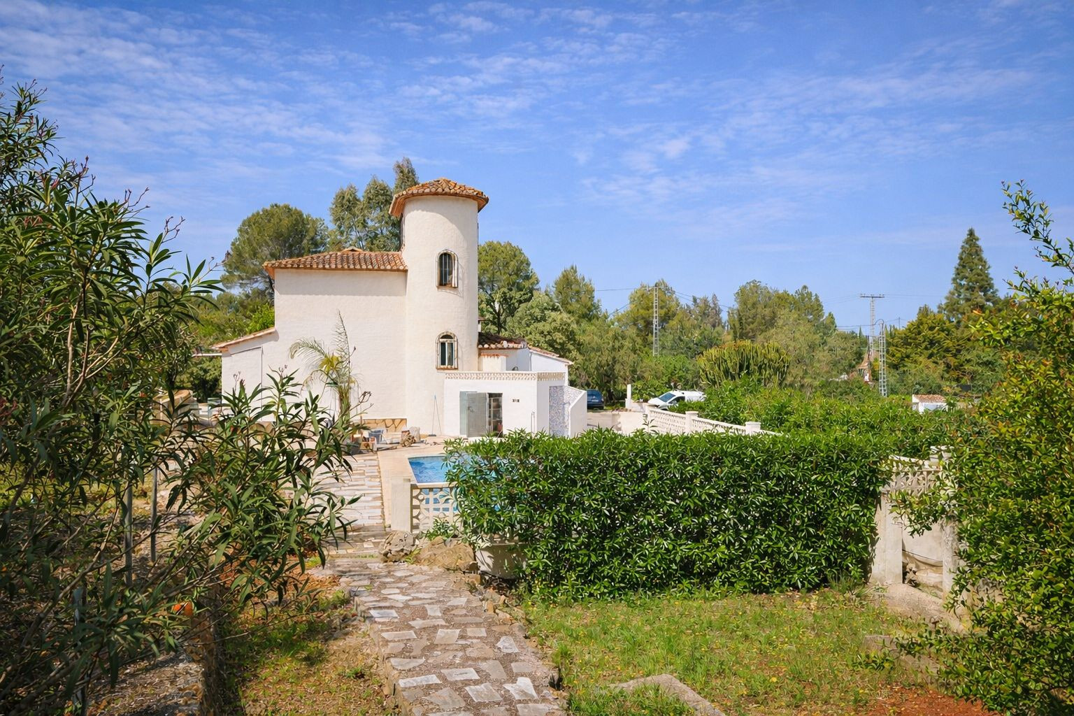 Außenansicht der Villa mit markantem Rundturm, Ziegeldach und mediterranem Garten mit Steinpfaden und privatem Poolbereich.