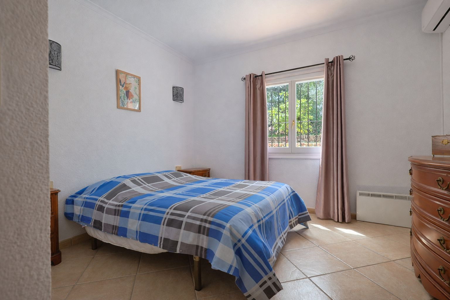Helles Schlafzimmer mit Fliesenboden, klassischen Holzmöbeln und Gartenblick. Ausgestattet mit Klimaanlage und elektrischer Wandheizung.