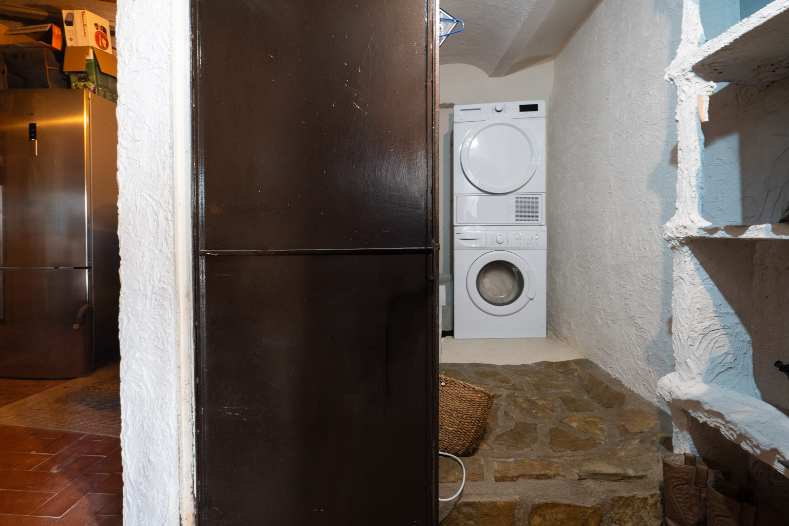 Funktionaler Hauswirtschaftsraum mit Waschmaschine und Trockner-Säule, strukturierten Wänden und einem rustikalen Natursteinboden.