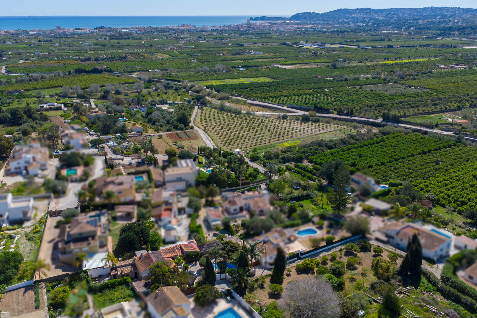 Luftaufnahme der Immobilie inmitten von Obstgärten, mit Blick auf die Mittelmeerküste und die Bucht von Jávea am Horizont.