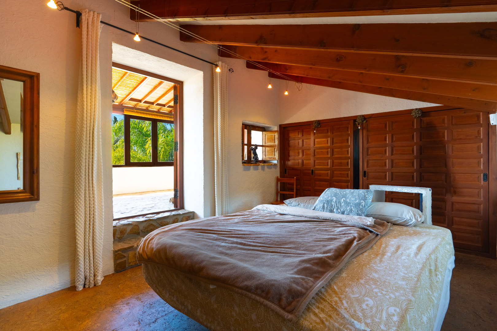 Schlafzimmer mit rustikalen Holzbalkendecken, Einbauschränken und direktem Zugang zu einer Terrasse mit Blick auf die umliegende Vegetation.