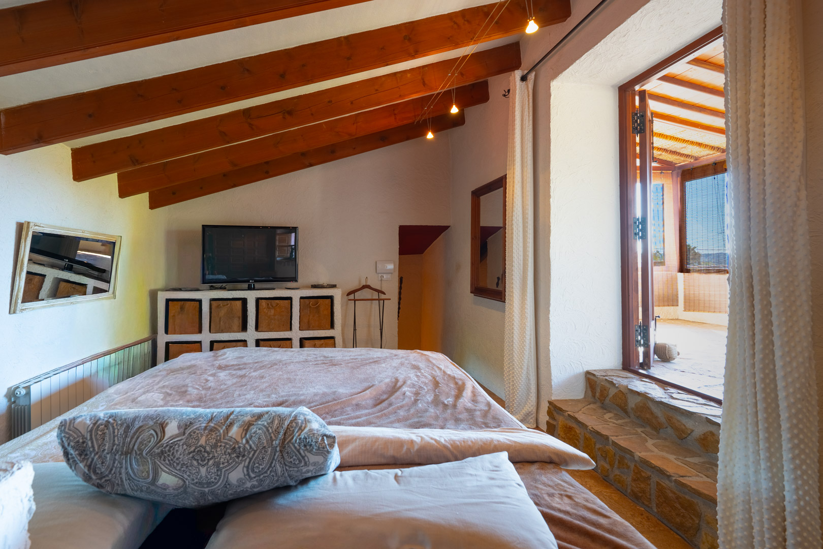 Schlafzimmer mit sichtbaren Holzbalken und Natursteinstufen, die einen direkten Zugang zur verglasten Naya ermöglichen.