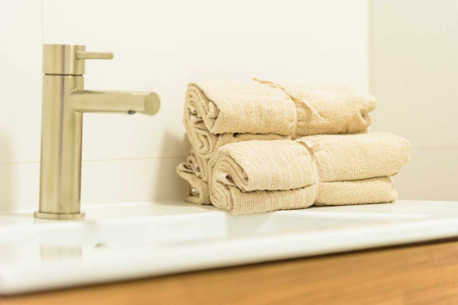 Detailansicht des Badezimmers mit gebürsteter Edelstahlarmatur, weißem Waschbecken und beigen Handtüchern auf einem modernen Holzunterschrank.