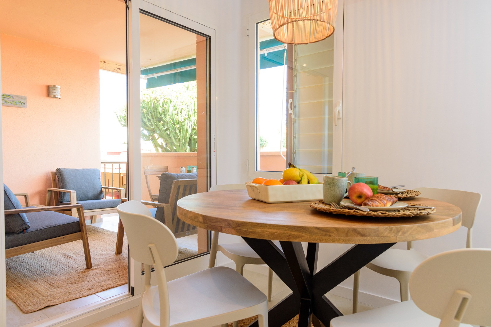 Heller Essbereich mit rundem Holztisch und weißen Stühlen, der durch große Glasschiebetüren direkt auf die möblierte Terrasse mit Außenbestuhlung führt.