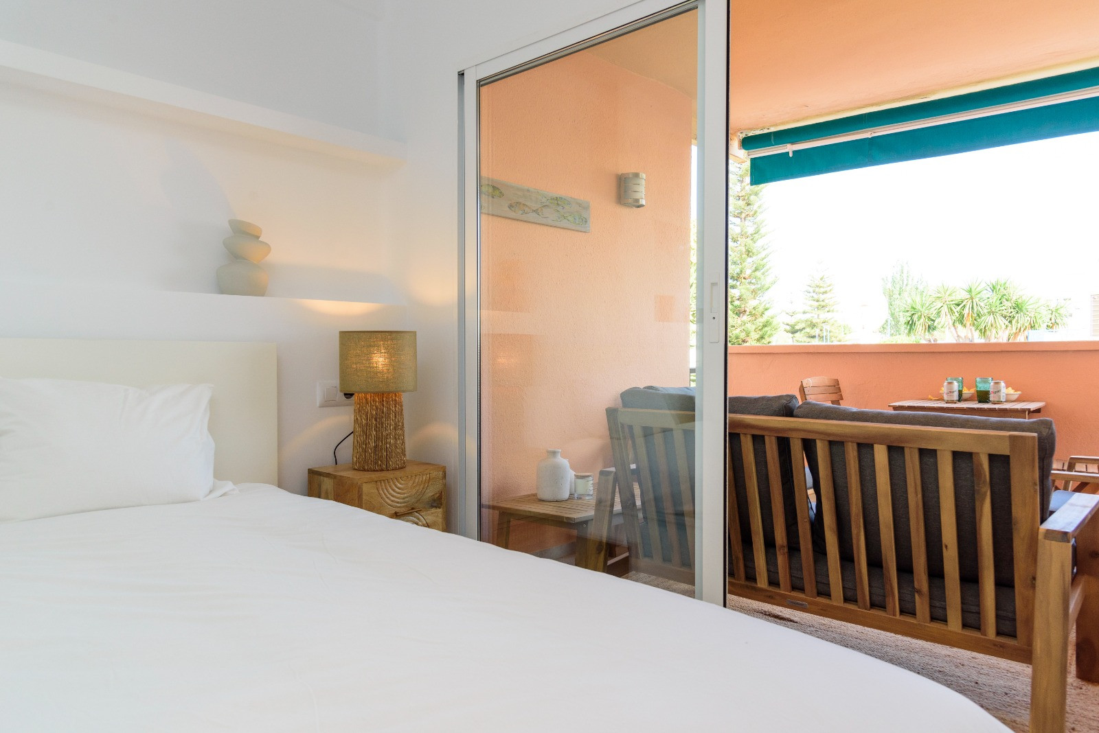 Helles Schlafzimmer mit direktem Zugang zu einer privaten Terrasse mit Holzmöbeln. Der Raum besticht durch natürliches Licht und ein minimalistisches Design.